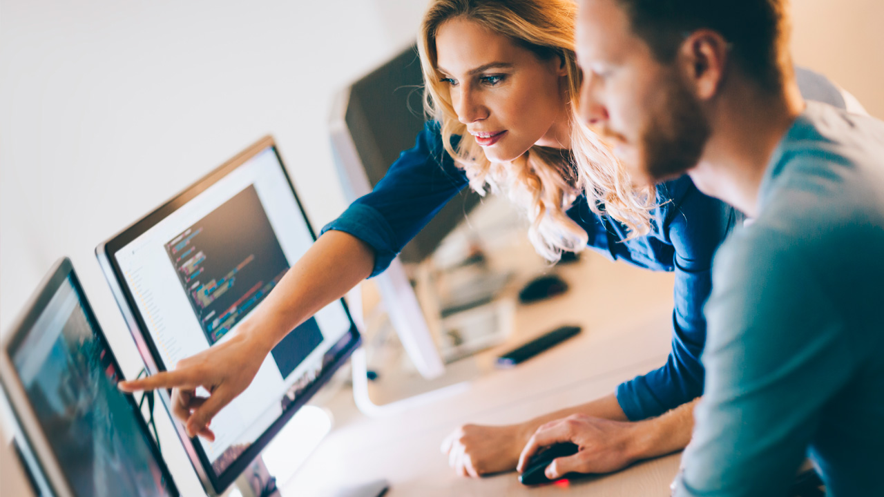 Duas pessoas, uma mulher e um homem, trabalhando em conjunto vendo gráficos em um computador.