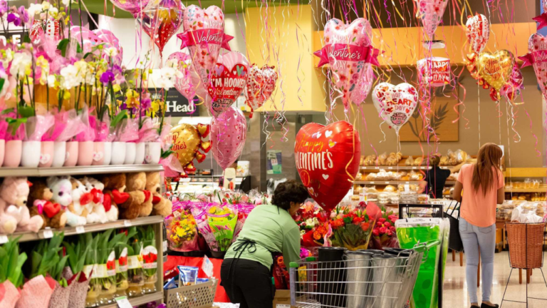 imagem ampla de um supermercado todo decorado para o Dia dos Namorados. Na imagem há vários balões vermelhos e cor-de-rosa, em formato de coração com mensagens apaixonadas.