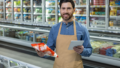 Um homem em um supermercado segurando um pacote em uma mão e um tablet na outra, fazendo o abastecimento automático de alimentos.