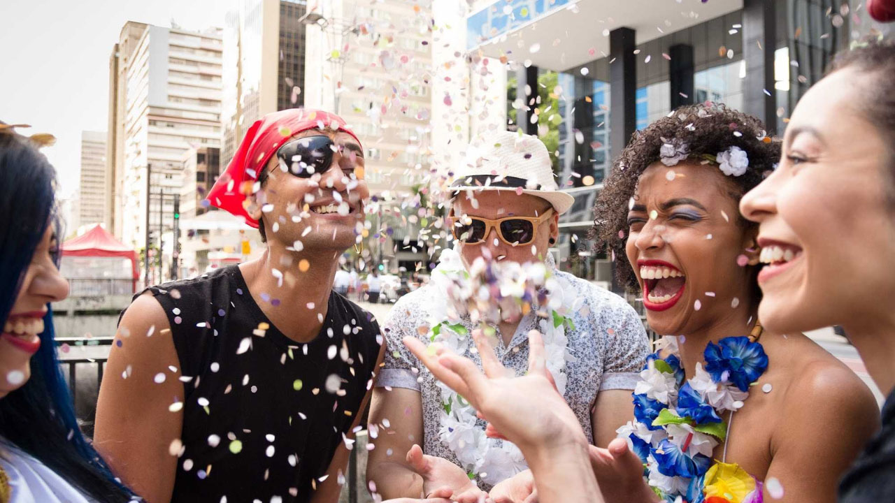 Foliões fantasiados para o carnaval e confetes entre eles. Criar ofertas de carnaval no seu supermercado é uma boa ideia para atrair clientes e vender mais.