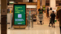 Retail media em ação: painel digital em supermercado comunica check-in seguro aos clientes.